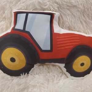 May include: Red and black tractor-shaped cushion with a white background. The tractor has a large front tyre and a smaller back tyre.