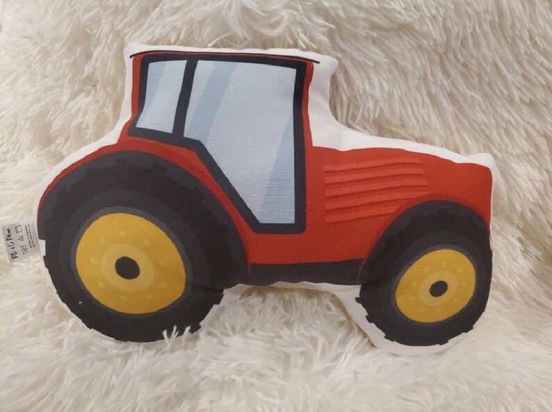 May include: Red and black tractor-shaped cushion with a white background. The tractor has a large front tyre and a smaller back tyre.