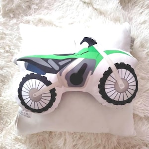 May include: A white pillow with a green and black motocross bike design. The bike has a black seat and black wheels with white spokes.