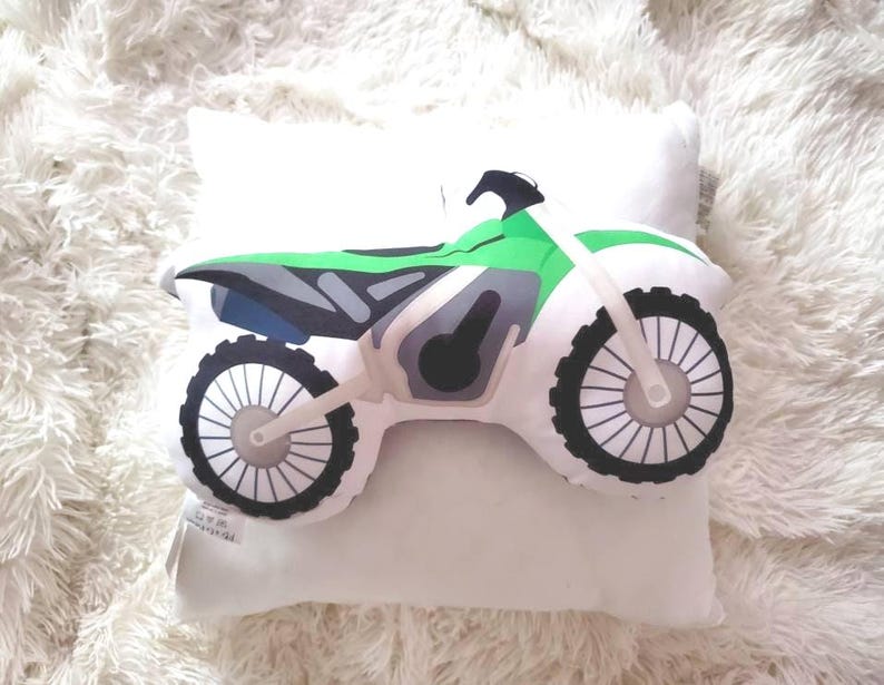 May include: A white pillow with a green and black motocross bike design. The bike has a black seat and black wheels with white spokes.