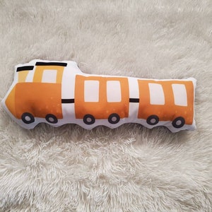 Peut inclure: Un jouet en peluche en forme de train avec des détails orange et blancs. Le train a cinq fenêtres et six roues.