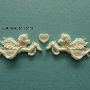 May include: Ivory-colored cherub figurines with outstretched wings and flowing fabric, each holding a ribbon. A small heart-shaped accent piece is also present. The text on the image indicates the cherubs are 7.5cm long, 4cm wide, and 7mm thick.