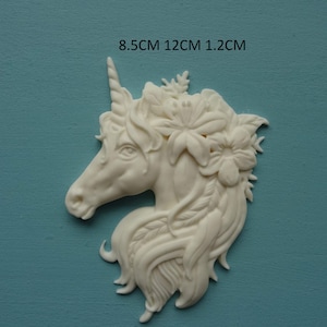 Op de afbeelding: Witte eenhoorn taarttopper met bloemdetails. De eenhoorn is 8,5 cm hoog, 12 cm breed en 1,2 cm dik.