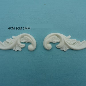 May include: Two white, decorative, ornate, scroll-shaped, leaf-like, floral embellishments with a 6 cm length, 2 cm width, and 5 mm thickness.  6CM 2CM 5MM.