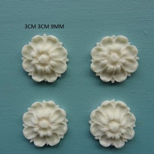 May include: Four white, 3 cm by 3 cm, decorative floral embellishments with a raised design.  3CM 3CM 9MM