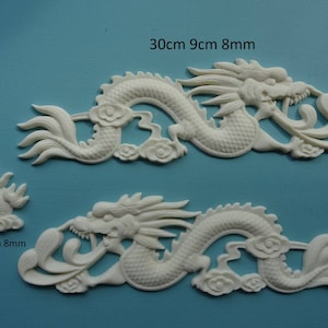 May include: Two white ceramic dragon wall decor pieces. The larger dragon is 30 cm long, 9 cm wide, and 8 mm thick. The smaller dragon is 6.5 cm long, 6 cm wide, and 8 mm thick.