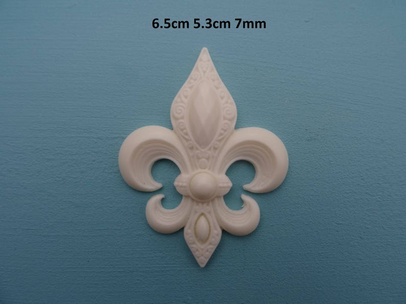 May include: White plastic fleur-de-lis ornament, 6.5cm x 5.3cm x 7mm.