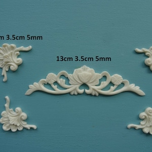 May include: Five white decorative mouldings for crafts or home decor. The mouldings are in the shape of floral designs. The largest moulding is 13 cm long and 3.5 cm wide. The smaller mouldings are 3.5 cm long and 3.5 cm wide. All mouldings are 5 mm thick.