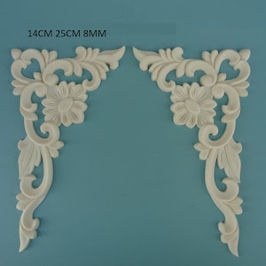 Puede incluir: Dos molduras de esquina blancas y ornamentadas con un diseño floral. Cada moldura mide 14 cm por 25 cm por 8 mm.