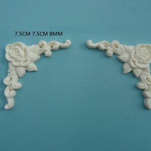 May include: Two white corner mouldings with a rose and leaf design. Each moulding measures 7.5 cm by 7.5 cm and is 8 mm thick.