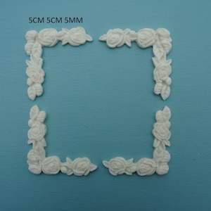 May include: Four white, 5 cm floral corner pieces for crafting or decorating. The pieces are made of a smooth, white material and feature a delicate floral design.