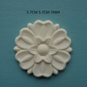 May include: White, decorative, floral-shaped wall decor with a raised design. The decor measures 5.7 cm in diameter and 7 mm in height.