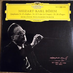 May include: A black and white photo of a conductor holding a baton, with the text "MOZART KARL BÖHM" in yellow letters on a black background. The text "Symphonien Nr. 35 Haffner - Nr. 32 G-dur (in G major). Nr. 38 Prager" is also in yellow letters on a black background. The text "BERLINER PHILHARMONIKER" is in yellow letters on a black background. The text "STEREO" is in yellow letters on a black background.