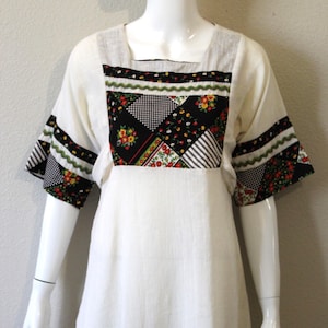 May include: A white vintage dress with a patchwork design on the bodice. The bodice features a black and white checkered pattern, floral print, and stripes. The dress has a square neckline and short sleeves with floral trim.