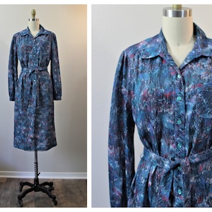May include: A long-sleeved dress with a button-down front and a matching belt. The dress features a teal, blue, and purple abstract pattern. The dress is displayed on a mannequin.