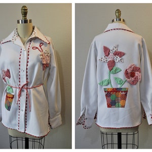 Peut inclure: Chemise boutonnée blanche avec bordure rouge et une applique de fleur en patchwork au dos. La fleur est dans un pot avec un motif patchwork.