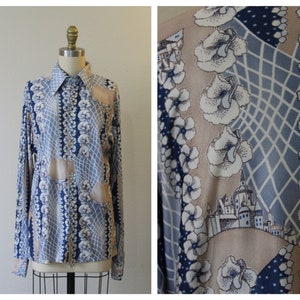 May include: A long-sleeved shirt with a geometric pattern in shades of blue, beige, and white. The pattern features stylized flowers and a cityscape.