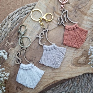 Könnte beinhalten: Drei Schlüsselanhänger aus Holz in Form eines Halbmondes mit den Anfangsbuchstaben S, E und M. Jeder Schlüsselanhänger hat einen Quasten aus weißem oder pfirsichfarbenem Garn.