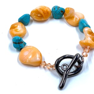 May include: A bracelet featuring alternating polished, light orange-colored stones and turquoise-colored stones. The bracelet is secured with a dark metal toggle clasp and has small, light orange beads near the clasp.