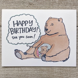 May include: A brown bear with a thought bubble that says "Happy Birthday! See you soon!" The bear is sitting with its legs crossed and has a smaller bear cub inside its belly.