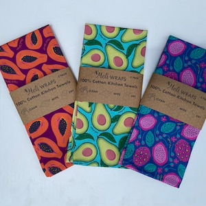 May include: Three cotton kitchen towels with different fruit designs. The towels are folded and have a brown label with the text "Meli Wraps 2 pack 100% Cotton Kitchen Towels Clean Wipe Dry".