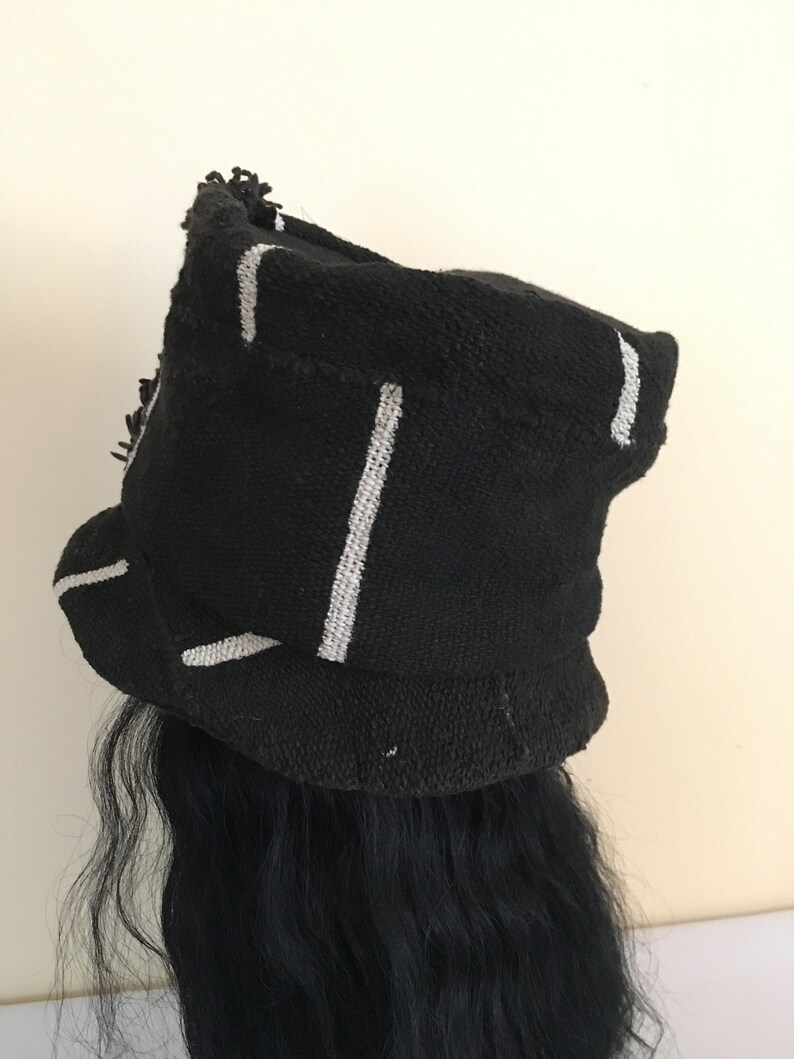 May include: Black knit hat with white vertical stripes. The hat has a rounded crown and a brim. The hat is worn over black hair. The hat has a textured appearance.