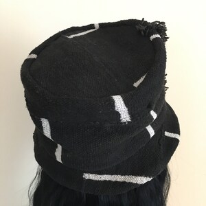 May include: Black hat with white stripes. The hat has a rounded crown and a small brim. The hat is made of a textured fabric and has a fringe detail along the edge. The hat is a stylish accessory.