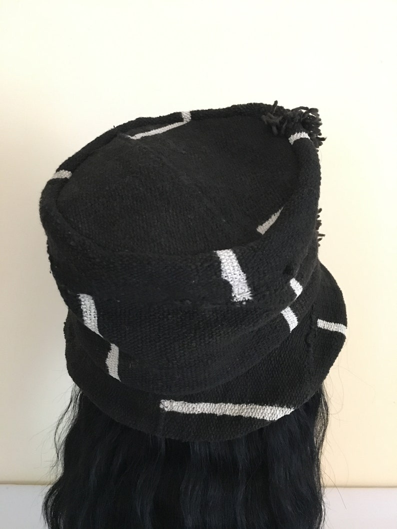 May include: Black hat with white stripes. The hat has a rounded crown and a small brim. The hat is made of a textured fabric and has a fringe detail along the edge. The hat is a stylish accessory.