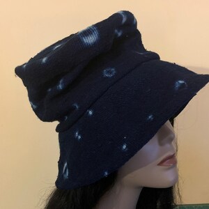Puede incluir: Un sombrero de pescador azul marino con patrones circulares blancos. El sombrero tiene un ala ancha y una corona ligeramente arrugada. La tela parece texturizada. El sombrero se muestra en una cabeza de maniqu&iacute;.