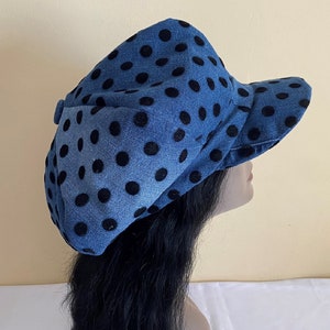 May include: A denim blue hat with large black polka dots. The hat has a brim and a rounded crown. The hat is made of a soft fabric and is likely for sun protection or fashion.