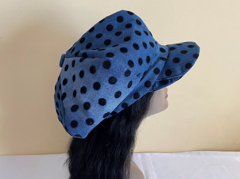 May include: A denim blue hat with large black polka dots. The hat has a brim and a rounded crown. The hat is made of a soft fabric and is likely for sun protection or fashion.