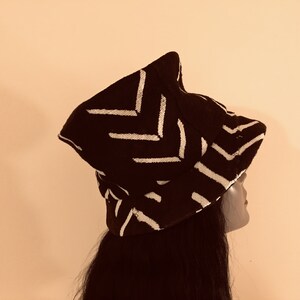 May include: A black hat with a white chevron pattern. The hat has a distinctive shape and is worn by a person with long, dark hair. The hat's design is a striking contrast of black and white.