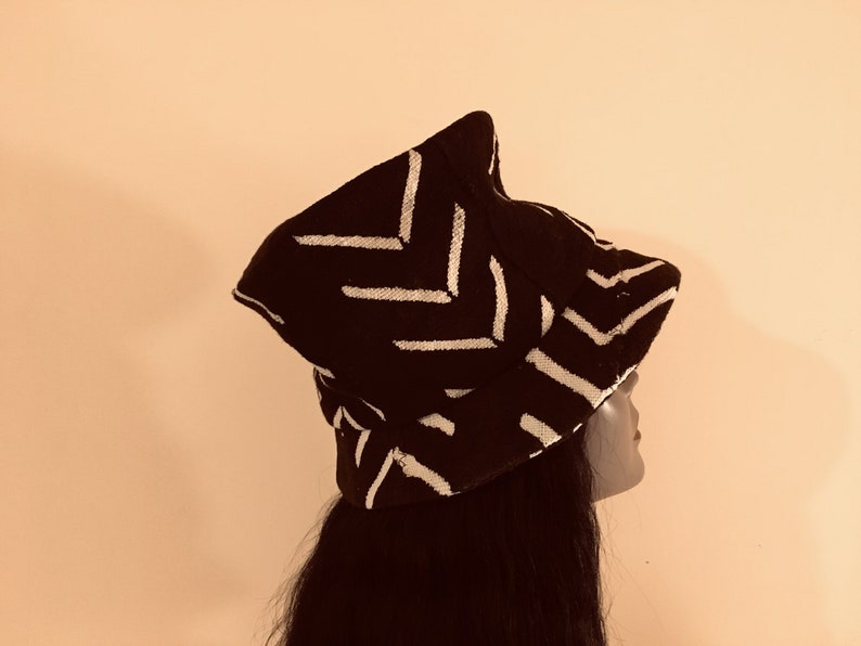 May include: A black hat with a white chevron pattern. The hat has a distinctive shape and is worn by a person with long, dark hair. The hat's design is a striking contrast of black and white.