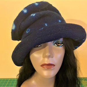 Puede incluir: Un sombrero azul oscuro con ala ancha y copa redonda. El sombrero presenta un patr&oacute;n de puntos azul claro. El sombrero est&aacute; hecho de una tela suave y texturizada. El sombrero se exhibe en una cabeza de maniqu&iacute; con cabello negro largo.