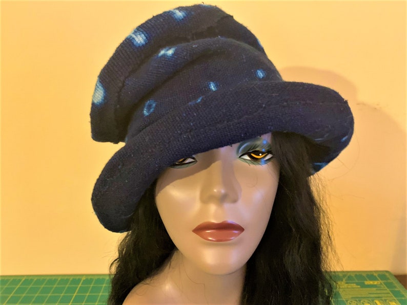 Puede incluir: Un sombrero azul oscuro con ala ancha y copa redonda. El sombrero presenta un patr&oacute;n de puntos azul claro. El sombrero est&aacute; hecho de una tela suave y texturizada. El sombrero se exhibe en una cabeza de maniqu&iacute; con cabello negro largo.