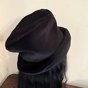 May include: A dark navy blue velvet hat with a rounded crown and a wide brim. The hat is made of a soft, plush material and has a classic, elegant design. The hat is a stylish accessory.