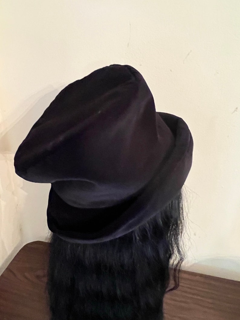 May include: A dark navy blue velvet hat with a rounded crown and a wide brim. The hat is made of a soft, plush material and has a classic, elegant design. The hat is a stylish accessory.