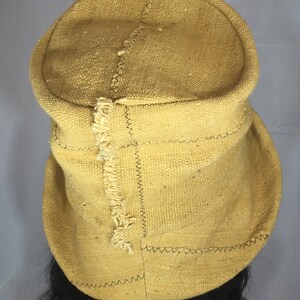 May include: Mustard yellow fabric hat with a rounded crown and a brim that folds up. The hat is constructed with visible stitching and has a textured appearance. The hat is a unique accessory.