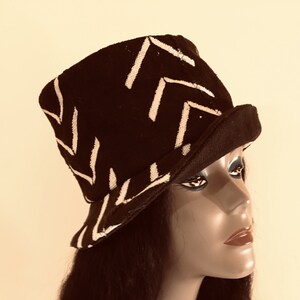 May include: A black hat with a white chevron pattern. The hat has a short brim and a structured crown. The hat is displayed on a mannequin head. The hat is a fashion accessory.