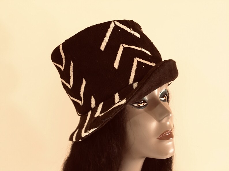 May include: A black hat with a white chevron pattern. The hat has a short brim and a structured crown. The hat is displayed on a mannequin head. The hat is a fashion accessory.