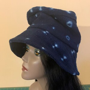 Puede incluir: Un sombrero de pescador azul marino con patrones circulares blancos. El sombrero tiene un ala ancha y una apariencia ligeramente arrugada. La tela parece ser un algod&oacute;n o lino texturizado. El sombrero se muestra en una cabeza de maniqu&iacute;.