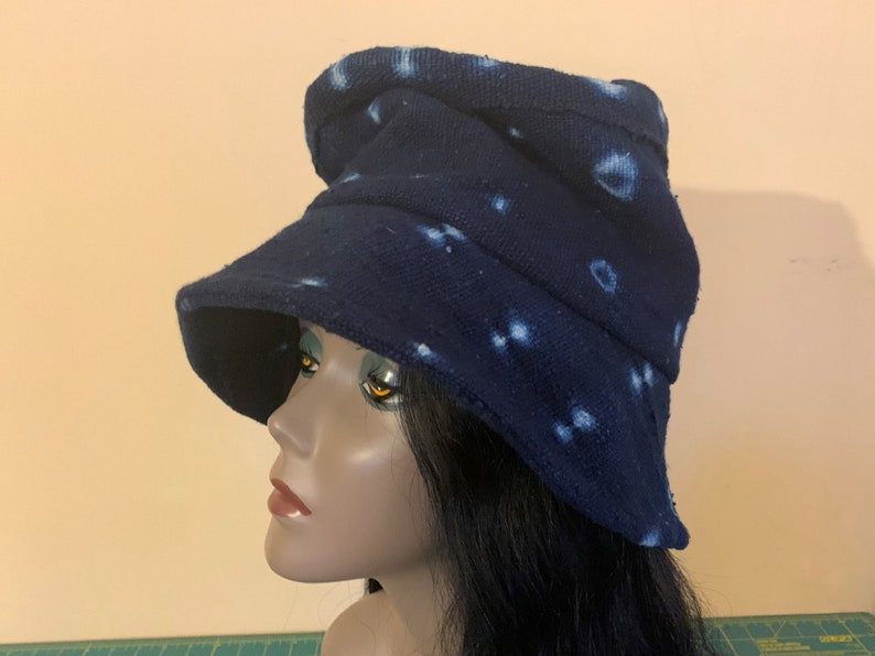 Puede incluir: Un sombrero de pescador azul marino con patrones circulares blancos. El sombrero tiene un ala ancha y una apariencia ligeramente arrugada. La tela parece ser un algod&oacute;n o lino texturizado. El sombrero se muestra en una cabeza de maniqu&iacute;.