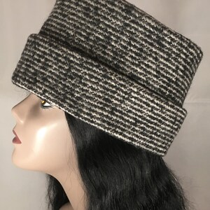 May include: A black and white patterned hat with a rectangular crown and a folded brim. The hat is made of a textured fabric and is displayed on a mannequin head. The hat's design features a diagonal stripe pattern.