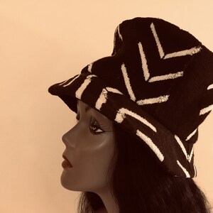 May include: A black bucket hat with a white geometric pattern. The hat is made of a textured fabric and features a brim. The hat is displayed on a mannequin head.