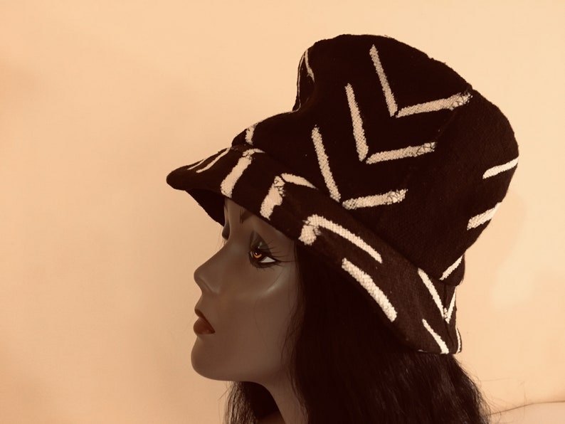 May include: A black bucket hat with a white geometric pattern. The hat is made of a textured fabric and features a brim. The hat is displayed on a mannequin head.