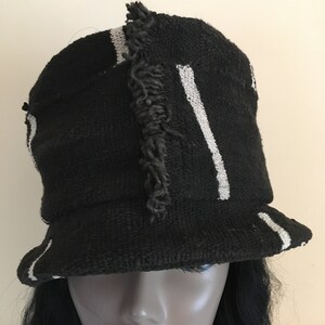 May include: Black bucket hat with white stripes and a frayed accent. The hat has a brim and is made of a woven material. A stylish accessory for sun protection or fashion.