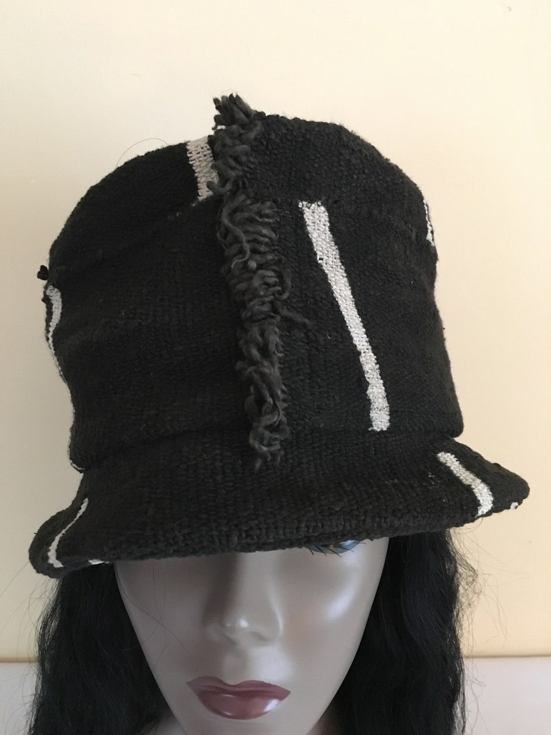 May include: Black bucket hat with white stripes and a frayed accent. The hat has a brim and is made of a woven material. A stylish accessory for sun protection or fashion.