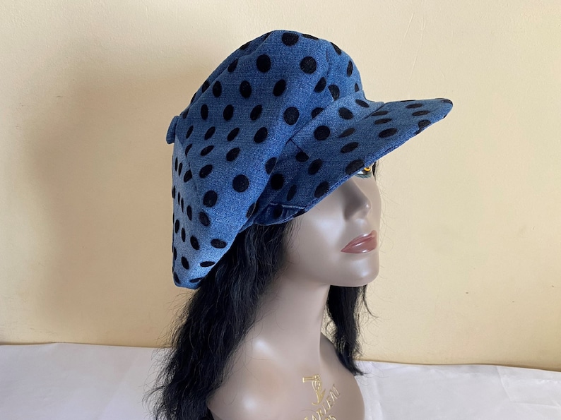 May include: Denim newsboy cap with a blue background and black polka dots. The cap has a rounded crown and a short, stiff brim. A stylish accessory for casual wear.