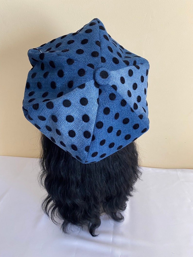 May include: A blue hat with black polka dots. The hat is made of a soft fabric and has a unique, geometric shape. The hat is a stylish accessory.