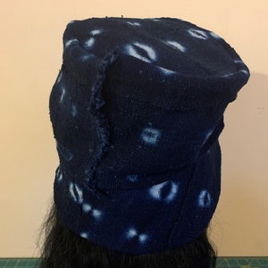Puede incluir: Un sombrero azul oscuro con ala, con un patr&oacute;n de dise&ntilde;os blancos en forma de ojo. El sombrero tiene un borde desgastado, lo que le da un aspecto artesanal. El sombrero est&aacute; hecho de una tela texturizada.